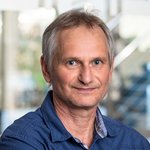 Dipl.-Ing. Holger Siegel, trägt ein blaues Hemd, steht in einem modernen Büro mit unscharfem Hintergrund.