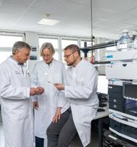 Drei Ärzte in weißen Kitteln diskutieren gemeinsam in einem Labor mit moderner Laborausrüstung