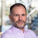 Marc Spiller, Mann mit kurzen grauen Haaren, trägt ein helles Hemd, sitzt in einem modernen Büro mit unscharfem Hintergrund.