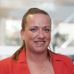 Katharina Depero trägt ein rotes Blazer-Jackett und steht vor einem unscharfen Hintergrund.