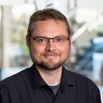 Dr. rer. nat. Sebastian Sahler, Toxikologie, trägt ein schwarzes Hemd, steht in einem modernen Büro mit unscharfem Hintergrund.